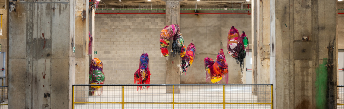 Various colourful textile sculptures hanging in an industrial concrete building.