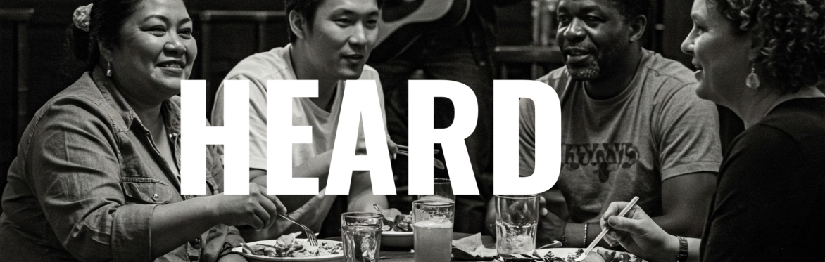 A group of people around a table enjoying a meal with the text "Heard"
