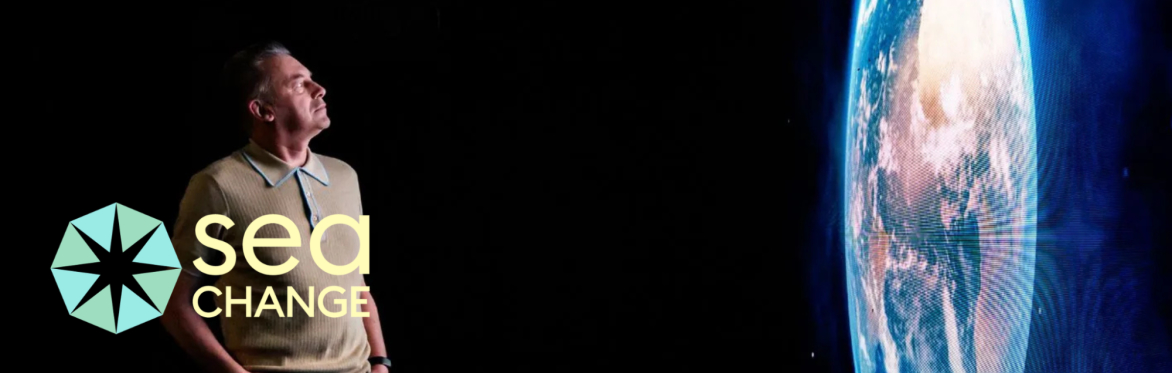 Man gazes thoughtfully at illuminated Earth image on dark background. "Sea Change" logo is visible in the bottom left corner