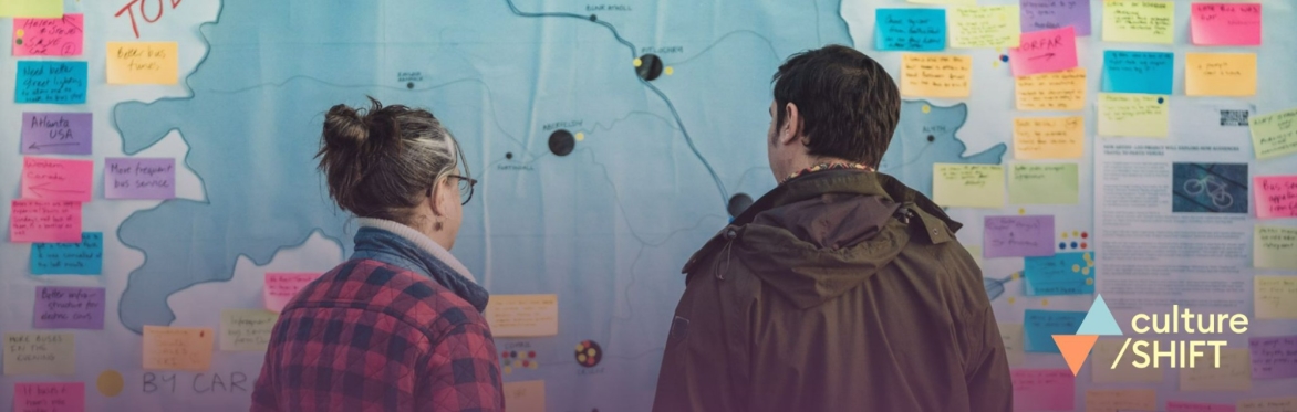 Two people looking at a large colourful map showing where people have travelled from