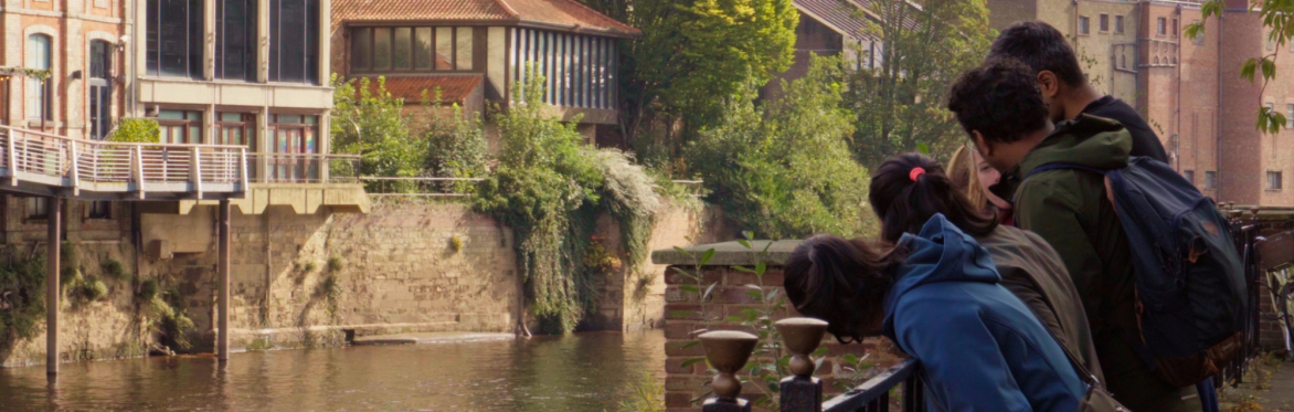 Young people standing beside the River Ouse, observing the water and riverside environment during a York rivers trail activity.