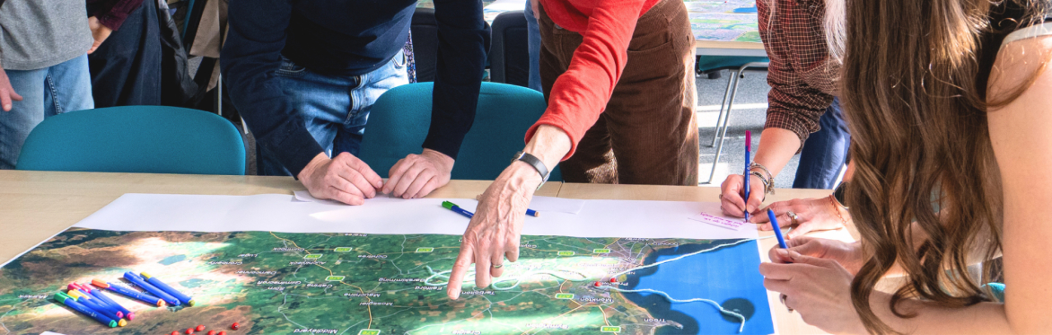 Four people stand around a map. One person points to a location.