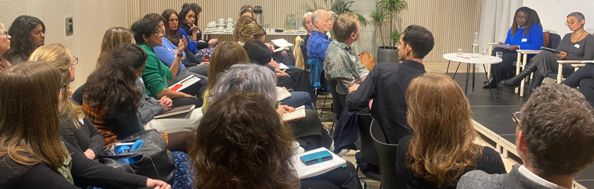 An audience of about 30 people are listening to a panel discussion