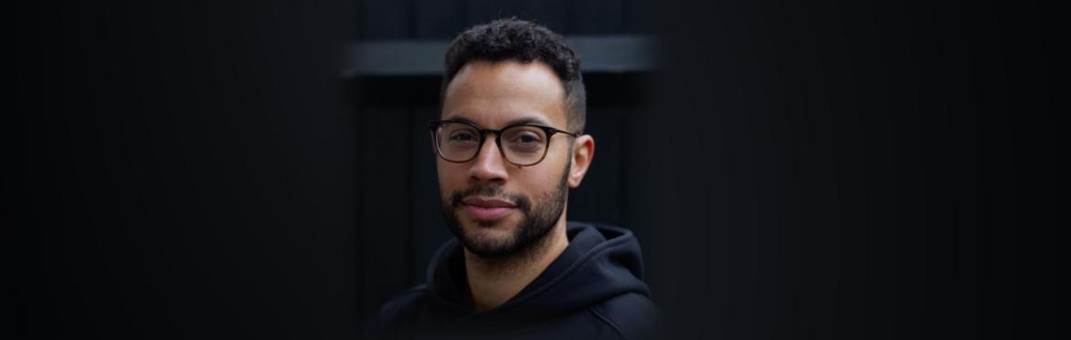 Lanre Bakare, a Black man with short hair and glasses, looks directly at the camera.