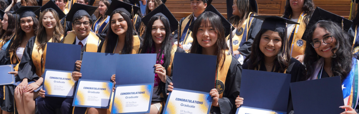 Students in their graduation cap and gown at the 2025 Herbert Wertheim School of Public Health and Human Longevity Science commencement. The students are sitting in a line holding certificates