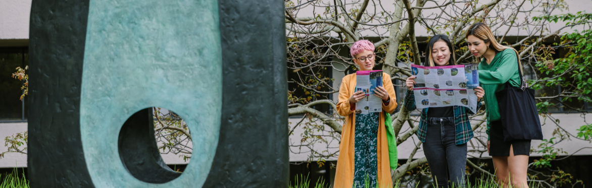 Three people looking at maps stood outside next to an oval shaped blue and black sculpture