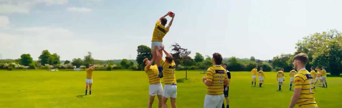 Rugby players lift a teammate to catch a ball during a lineout practice on a sunny field.