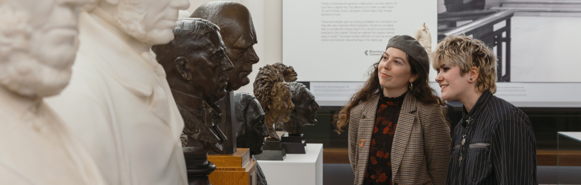 Two people looking at a row of portrait busts made of bronze and marble, stood on plinths