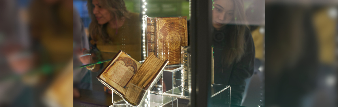 Two people looking at illuminated medieval books displayed in a lit glass museum case.
