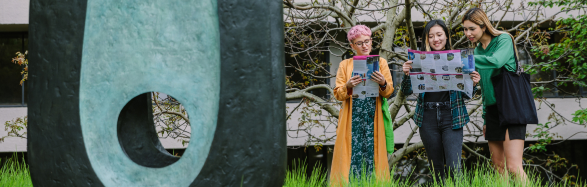Three people looking at maps stood outside next to an oval shaped blue and black sculpture