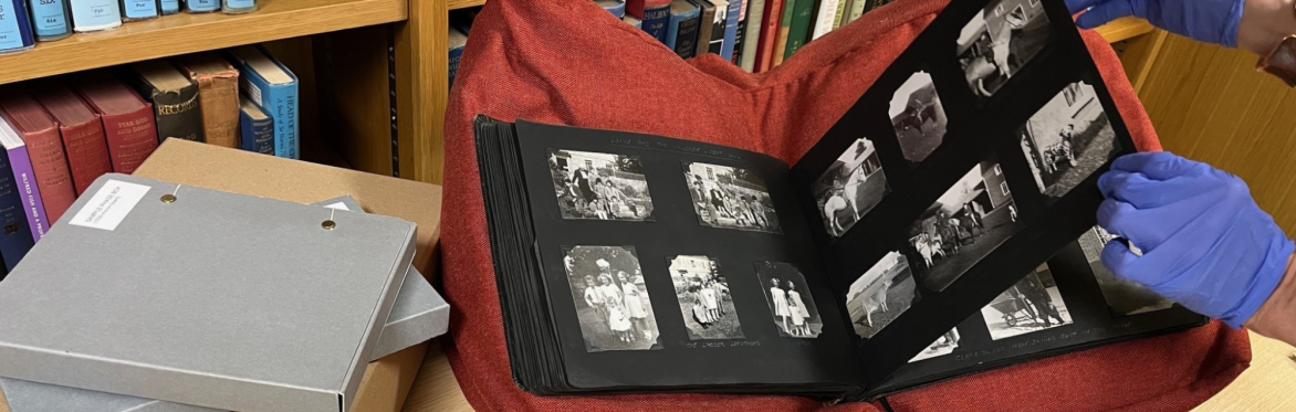 A photograph album on a book rest with a pair of gloved hands turning the pages. A variety of packaging materials next to the album