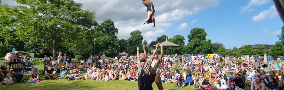a circus performer flipping high in the air above an audience seated on the grass