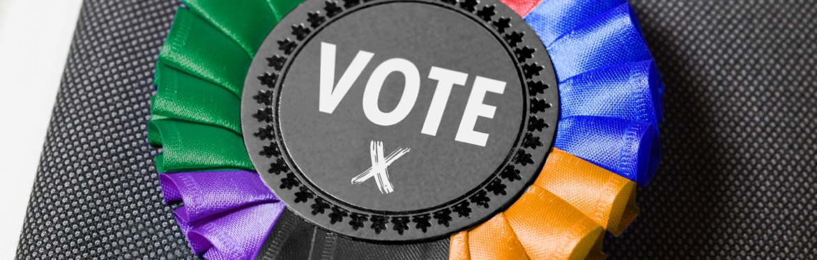Election candidate rosette pinned on a grey suite with multiple colours around the outside of the rosette