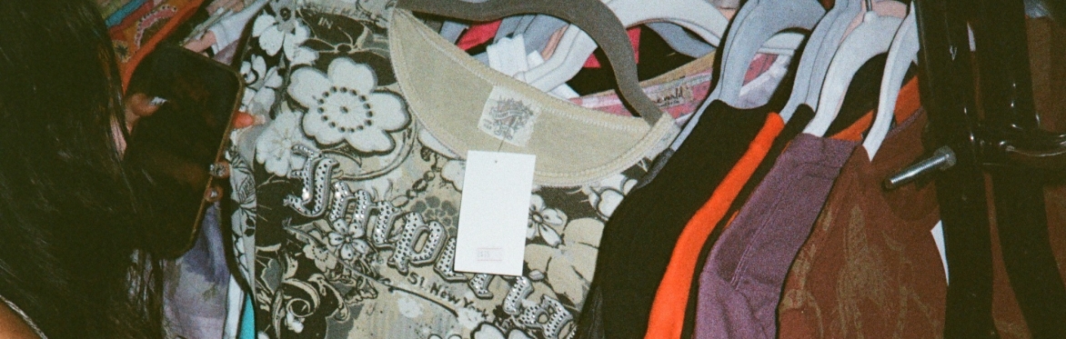 It is a photo of a person holding their phone looking at a t shirt they've selected on a clothing rack.