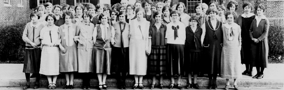Women office workers posing in front of a brick building in 1920s clothing