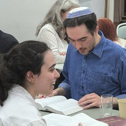 Close up of two people smiling and reading open books in Makom's storefront space