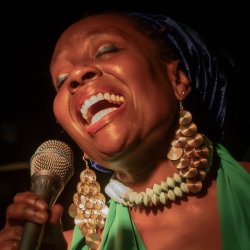 Black woman wearing headscarf, big jewellery and holding microphone