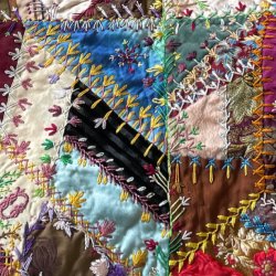 Close up view of a colorful crazy quilt with a variety of fabrics stitched together using colorful embroidery in various stitching patterns.