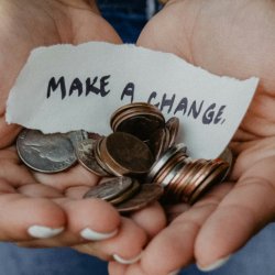 A close up of a woman cupping her hands with coins in it and a note saying make a change