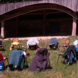 A circle of chairs in a field with people's belongings on in the sunshine