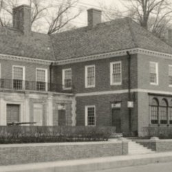 Black and white photo showing a streetscape with two large brick buildings in the Colonial Revival style.