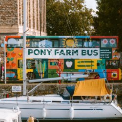 Photo of The Pony Farm Bus parked on Bristol Harbour outside Arnolfini, there are black and white marquees running alongside it for the market and boats in front on the water