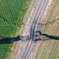 Aerial view of green fields with a dark crack running through them, crossing a railroad track. The image conveys tension and disruption.
