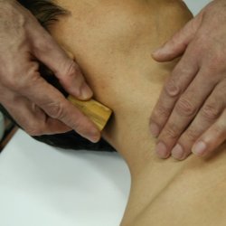 A practitioners hands during a warm bamboo treatment on someones neck.