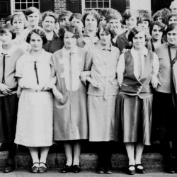 Women office workers posing in front of a brick building in 1920s clothing.