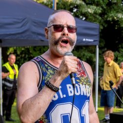 A man sings into a microphone at an outdoor event in a park.