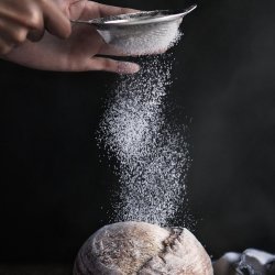 flour being sieved onto bread