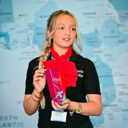 A female travel & tourism student is holding a product in front of a map of the world.