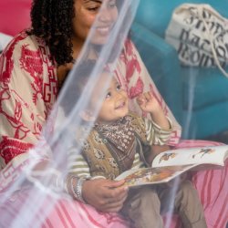 A young child and their carer smiling. The parent/carer is holding a small white ball