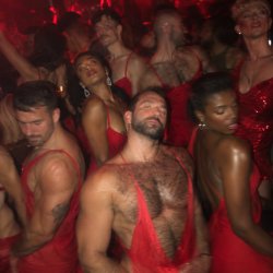 A variety of stylish people in red dresses at a discothèque.