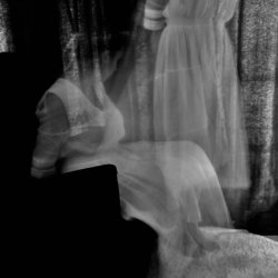 a blurred black and white image of a woman sitting and another standing right by her