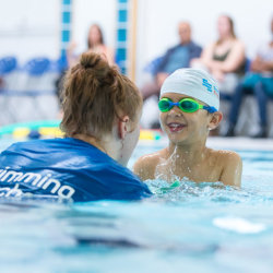 Assistant Swimming teacher helping  child in the water in a swimming lesson
