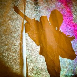 The shadow of a child behind textured material, their arms raised in the air