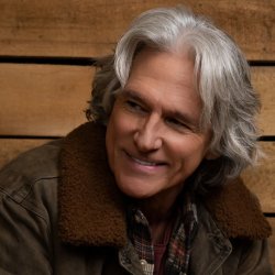 Billy Dean smiling in front of a wood panel background