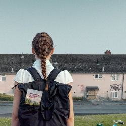 A teenage girl in school uniform looks at a row of houses. In the pocket of her backpack is a leaflet that says "Memorial of Jesus' Death"