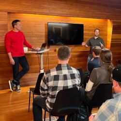 E-Commerce Growth Workshop: Operators Teaching Operators. Two presenters speak to a seated audience in a warm, wood-paneled event space.