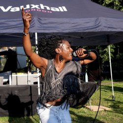 A woman sings into a microphone at an outdoor event in a park.