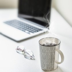 A mug of steaming tea, some spectacles, and a laptop