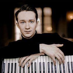 Accordionist Ryan Corbett with his instrument resting on his lap, black turtleneck, warm indoor portrait.