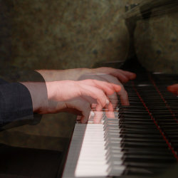 Hands on the keys of a grand piano, a double-exposure layering the pianist’s arms, at the JAM Festival.