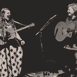 The image features Hannah Rarity and Anna Massie in sepia tones standing and performing while looking at each other with joyful expressions