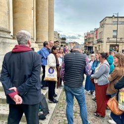 Woman standing with a tote bag next to a group of walking tour attendees next to Baliol College