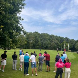 A group of golfers spectating a putting competition.