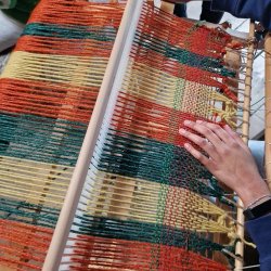 yarn is stretched over a loom and a hand prepares to add another row