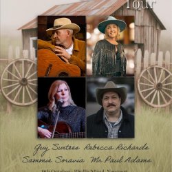 Four adults, two men and two women dressed in country attire. One man and one woman each holding an acoustic guitar.
