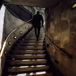 Silhouetted man walking up tube station staircase into the sun